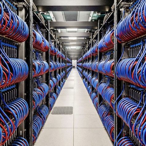Rows of server racks filled with neatly bundled blue and red network cables in a data center, forming a long aisle used for high-performance computing and network infrastructure.